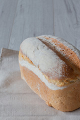 Farmhouse loaf of bread freshly baked on a tea towel with a grey wood background