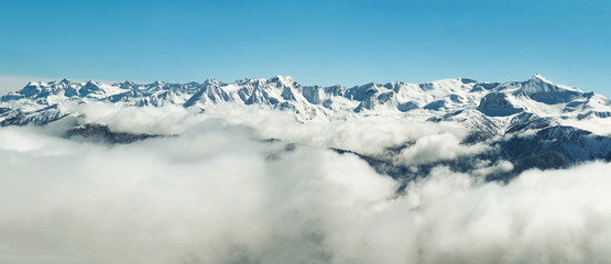 Panoramic view of winter snowy mountains range in clouds in Abkhazia at blue sky background
