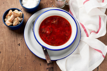 Bowl of red beetroot soup borscht with sour cream and bread crackers on rustic background