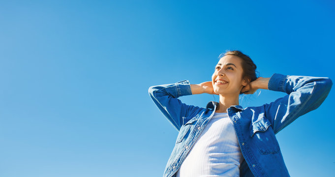 bottom view of a young smiling attractive woman in jeans clothes at sunny day on the blue sky background. joyful woman posing outdoors