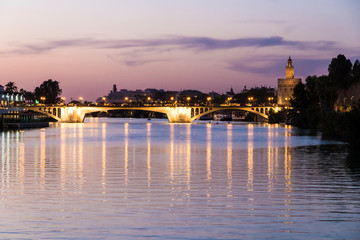 Fototapeta premium Sevilla, Spain. Views of the Guadalquivir river, with the Torre del Oro (Tower of Gold) and the Puente de San Telmo bridge at sunset