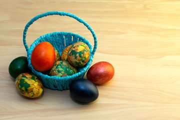Easter eggs lying on a yellow wooden table and in a blue basket, copy pastes