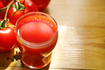 Tomato juice in a glass Cup with a bunch of ripe tomatoes, on a light wood background. Close up.copy space