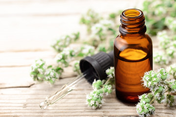 Marjoram essential oil in the glass bottle, with fresh marjoram flowers, on the wooden board