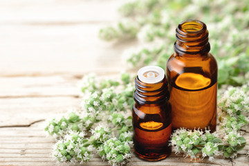 Marjoram essential oil in the glass bottle, with fresh marjoram flowers, on the wooden board