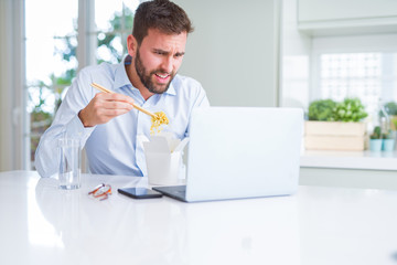 Business man eating take away asian noodles food while working using computer laptop and smiling