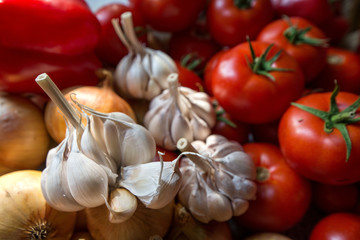 Ripe, fresh, harvested vegetables on table. Onions, tomatoes, garlic on kitchen table prepared to make a delicious vegetarian meal or for canning veggies for winter in jars. Concept of healthy eating