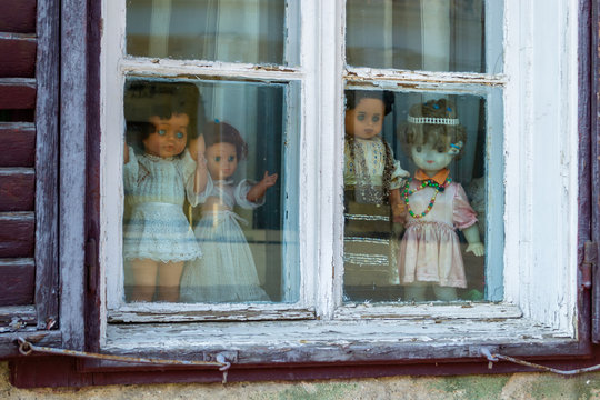 Four creepy dolls dressed in white and with traditional Romanian clothes, displayed in a window, while looking at the people passing by. Close up of puppets - horror concept.