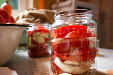 Fototapeta na wymiar Canning fresh tomatoes with onions in jelly marinade. Woman hands putting red ripe tomato slices and onion rings in jars. Basil, parsley leaves on top of onions. Vegetable salads for winter