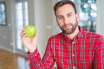 Handsome man eating fresh healthy green apple with a confident expression on smart face thinking serious