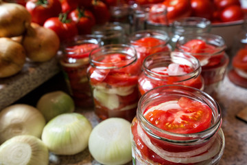 Canning fresh tomatoes with onions in jelly marinade. Woman hands putting red ripe tomato slices and onion rings in jars. Basil, parsley leaves on top of onions. Vegetable salads for winter