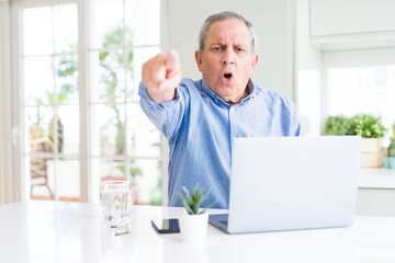 Handsome senior man using computer laptop working on internet pointing with finger to the camera and to you, hand sign, positive and confident gesture from the front