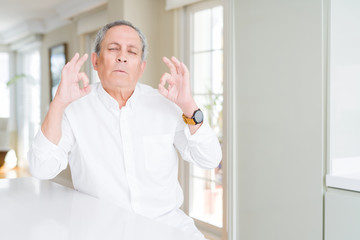 Fototapeta premium Handsome senior man at home relax and smiling with eyes closed doing meditation gesture with fingers. Yoga concept.