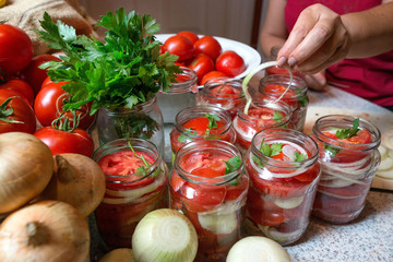 Canning fresh tomatoes with onions in jelly marinade. Woman hands putting red ripe tomato slices and onion rings in jars. Basil, parsley leaves on top of onions. Vegetable salads for winter