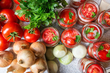 Canning fresh tomatoes with onions in jelly marinade. Woman hands putting red ripe tomato slices and onion rings in jars. Basil, parsley leaves on top of onions. Vegetable salads for winter