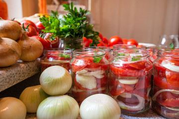 Canning fresh tomatoes with onions in jelly marinade. Woman hands putting red ripe tomato slices and onion rings in jars. Basil, parsley leaves on top of onions. Vegetable salads for winter