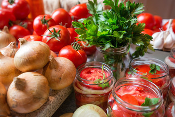 Canning fresh tomatoes with onions in jelly marinade. Woman hands putting red ripe tomato slices and onion rings in jars. Basil, parsley leaves on top of onions. Vegetable salads for winter