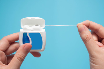 Close up of young female hands holding dental floss on blue background. Dental health care and oral...
