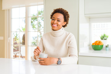 Beautiful young african american woman with afro hair drinking a cup of coffee at home