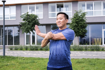 Fototapeta premium Korean man stretches against the background of the city. Healthy lifestyle. Adult man practicing yoga in nature.