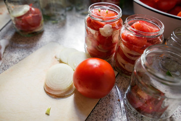 Canning fresh tomatoes with onions in jelly marinade. Woman hands putting red ripe tomato slices and onion rings in jars. Basil, parsley leaves on top of onions. Vegetable salads for winter