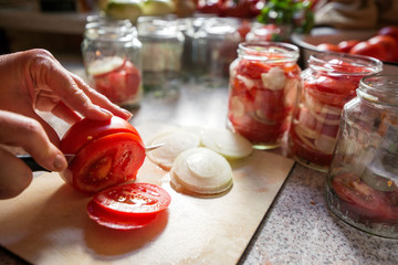Canning fresh tomatoes with onions in jelly marinade. Woman hands putting red ripe tomato slices and onion rings in jars. Basil, parsley leaves on top of onions. Vegetable salads for winter