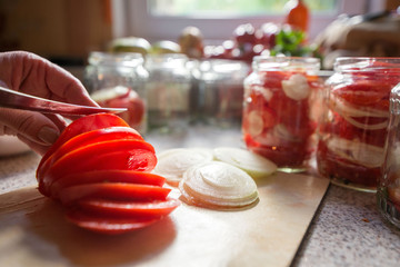 Canning fresh tomatoes with onions in jelly marinade. Woman hands putting red ripe tomato slices and onion rings in jars. Basil, parsley leaves on top of onions. Vegetable salads for winter