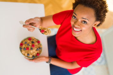Fototapeta premium Young beautiful african american woman with afro hair eating healthy wholemeal cereals and berries as healthy breakfast