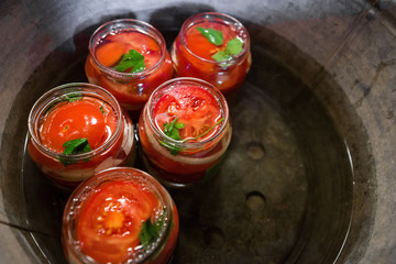 Canning fresh tomatoes with onions in jelly marinade. Conservation and cooking. Jars boiling in water to kill bacteria. Sealing process.  Basil, parsley leaves on top. Vegetable salads for winter