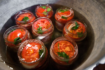 Canning fresh tomatoes with onions in jelly marinade. Conservation and cooking. Jars boiling in water to kill bacteria. Sealing process.  Basil, parsley leaves on top. Vegetable salads for winter