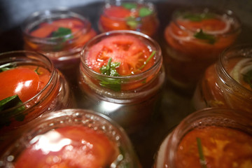 Fototapeta na wymiar Canning fresh tomatoes with onions in jelly marinade. Conservation and cooking. Jars boiling in water to kill bacteria. Sealing process. Basil, parsley leaves on top. Vegetable salads for winter
