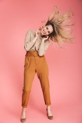 Full length portrait of stylish woman smiling and having fun isolated over pink background