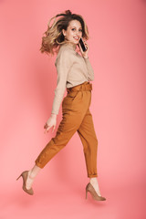 Full length portrait of pretty woman smiling and walking isolated over pink background