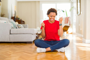 Young beautiful african american woman sitting on the floor at home very happy and excited doing winner gesture with arms raised, smiling and screaming for success. Celebration concept.