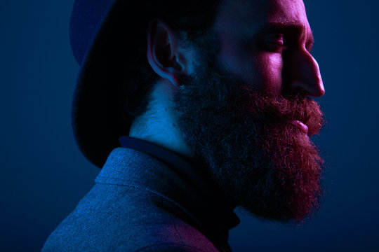 Close Up Portrait Of A Bearded Man In Hat And Suit, With Close Eyes Posing In Profile, On Dark Blue Background.