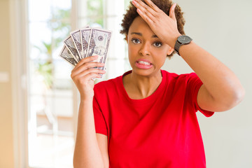 Young african american woman holding bank notes of fifty dollars stressed with hand on head, shocked with shame and surprise face, angry and frustrated. Fear and upset for mistake.