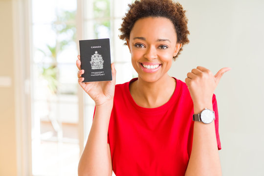 Young african american woman holding Canadian passport pointing and showing with thumb up to the side with happy face smiling