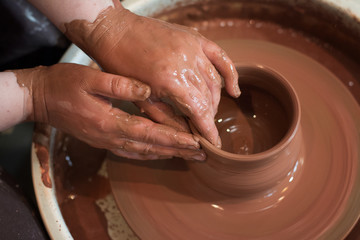 Rotating potter's wheel and clay ware on it taken from above. A sculpts his hands with a clay cup on a potter's wheel. Hands in clay. 