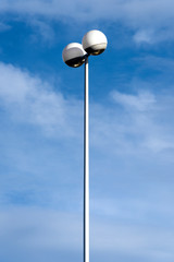 High tall lamp post streetlight with futuristic two spherical round light fixture on the upper end with blue sky and white clouds in the background - concept lantern illumination modern design future 