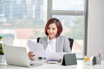 Happy asian woman working in office. Female going through some paperwork at work place.