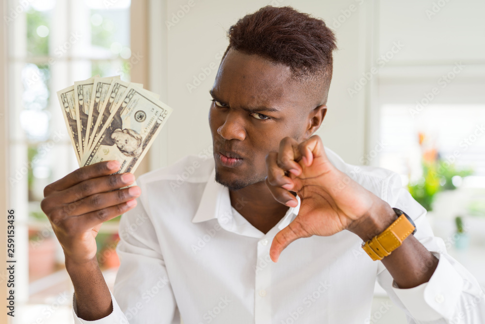 Poster African american man holding twenty dollars bank notes with angry face, negative sign showing dislike with thumbs down, rejection concept