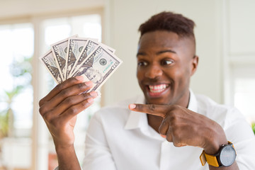 African american man holding fifty dollars bank notes very happy pointing with hand and finger