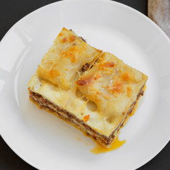 Traditional beef lasagne on a white round plate over black background, top view. Close-up.