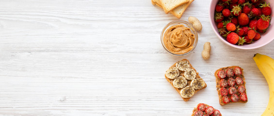 Healthy vegetarian breakfast with ingredients, diet concept. Vegan toasts with fruits, seeds, peanut butter on a white wooden table, top view. Copy space.