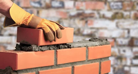 Photo sur Aluminium Mur de briques Worker builds a brick wall in the