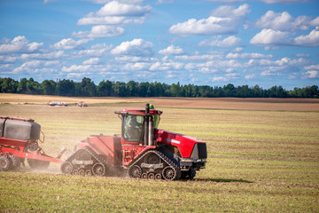 Agricultural background with red tractor pulling plow, throwing dust in air. Combine harvester at wheat field. Heavy machinery during cultivation, working on fields. Dramatic sky, rain, storm clouds
