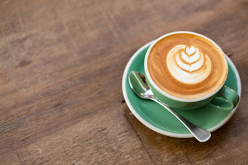 Latte hot coffee in a green cup with latte art and roasted coffee beans on wooden table background