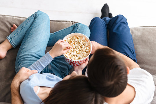 Image From Top Of Satisfied Couple Eating Popcorn From Bucket While Sitting On Couch Indoor And Watching Movie