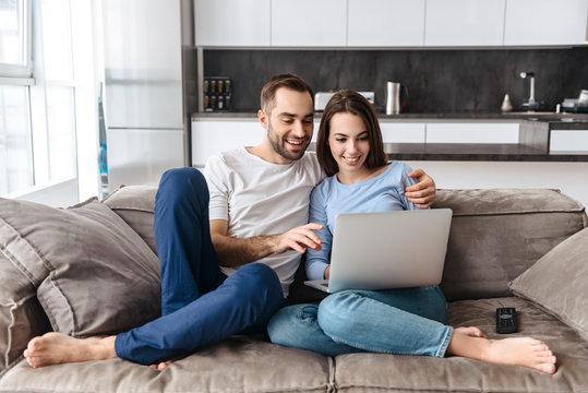Image of caucasian couple using laptop together while sitting on sofa in living room at home