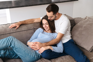 Image of caucasian pregnant woman and handsome man at home lying on sofa in living room